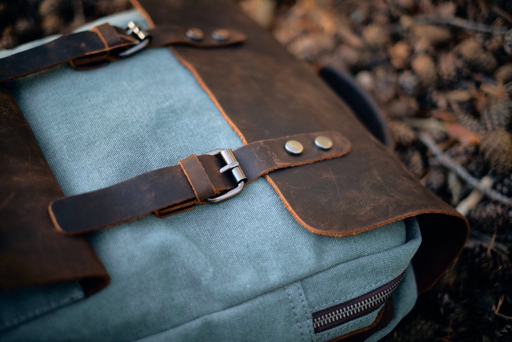 Light blue waxed canvas backpack with leather straps resting on the floor