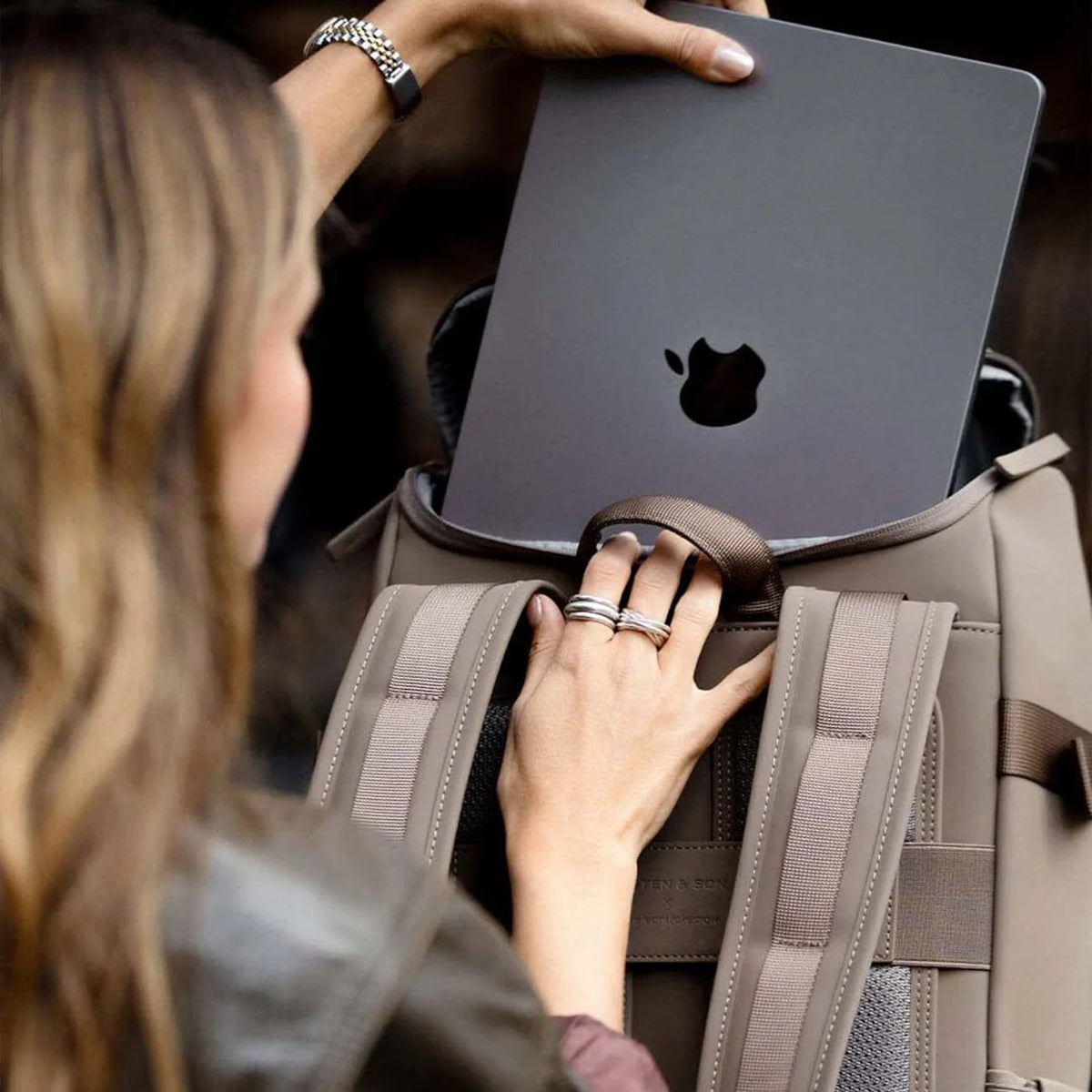 Woman sliding a MacBook into the walnut Bali Medium through the top opening