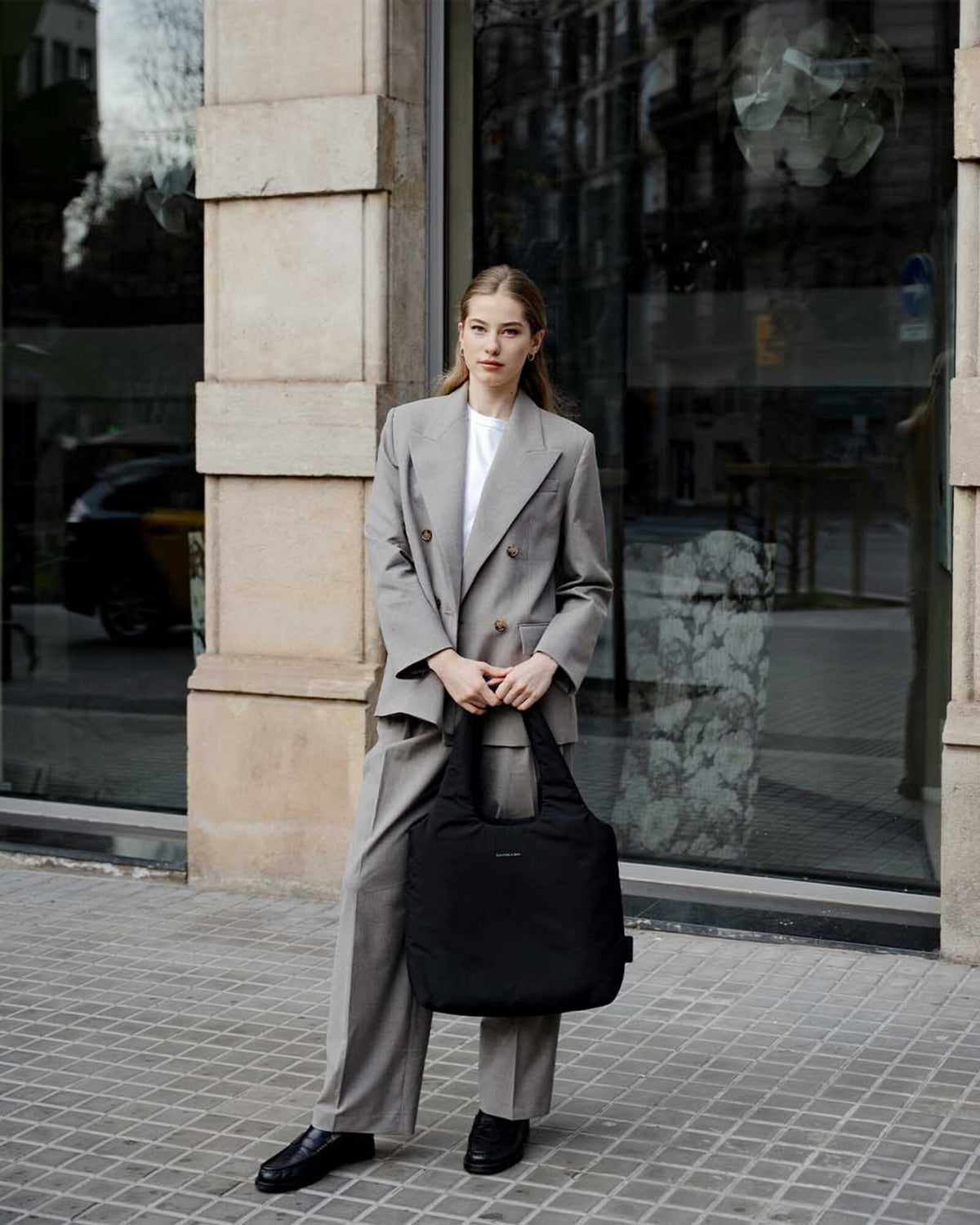 Woman holding the black Skara Cloud Tote by its handles in front of a shop window