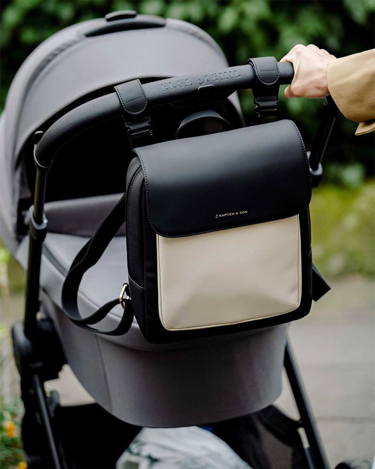 The cream black Kapten & Son Tromso Small hanging from a buggy handlebar