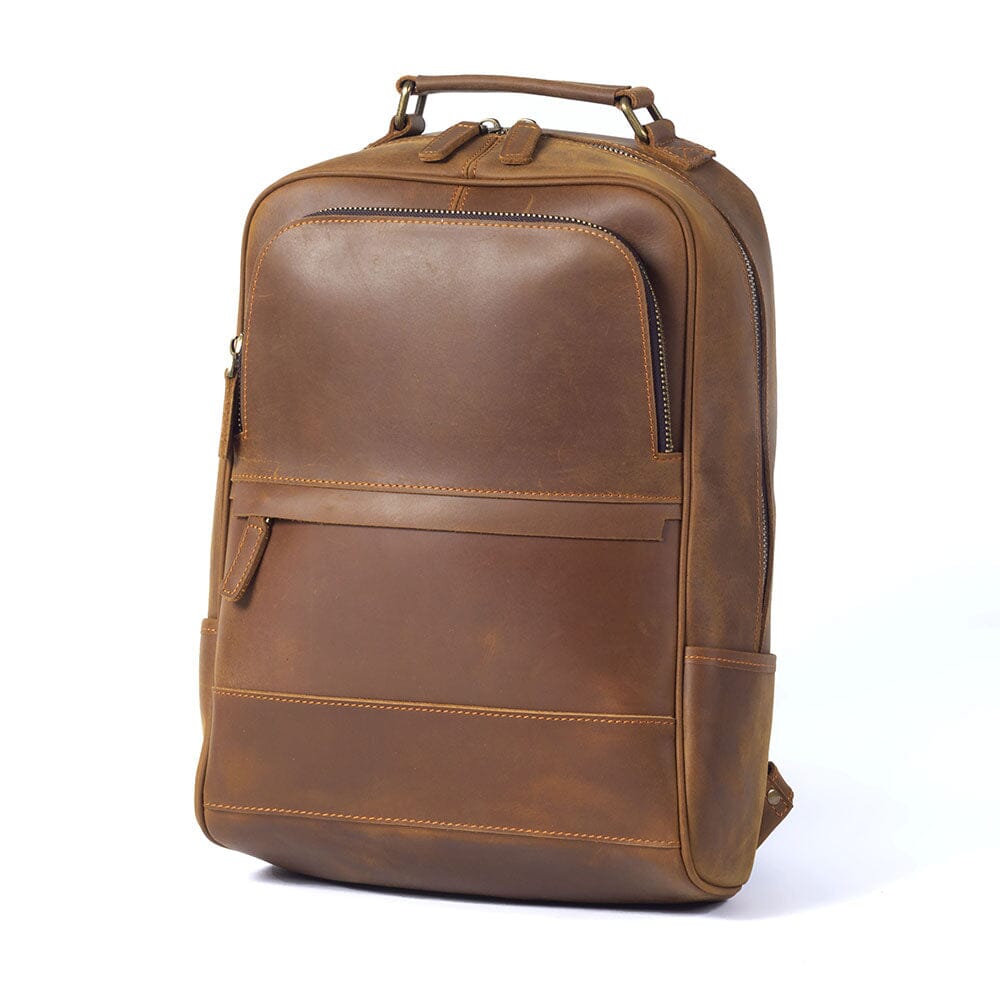 three quarter view of the light caramel leather backpack, twin zip pulls above the curved front pocket